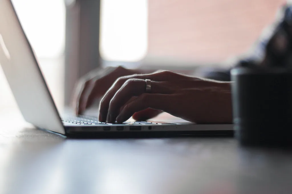 Hands typing on a laptop keyboard at a work desk